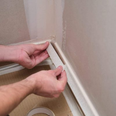 Unrecognizable painter using tape to cover the skirting board before painting.